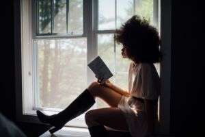 woman sitting on window sill reading book