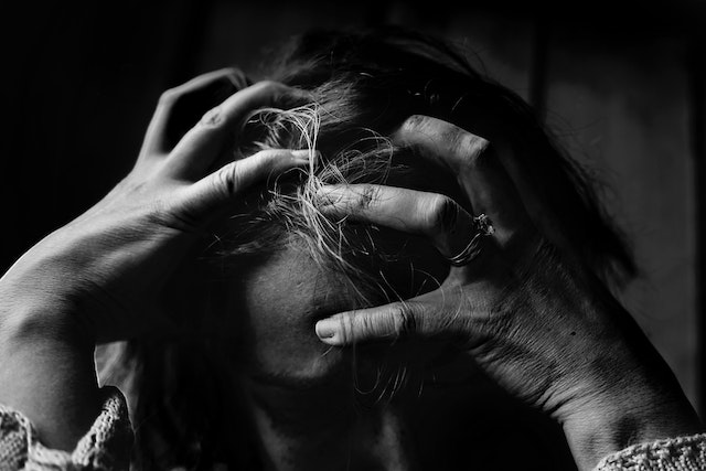and white image of woman who is stressed clenching her hands on her head