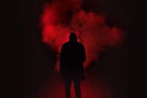 silhouette of a man standing with his back turned towards camera facing an ominous dark red fire and smoke