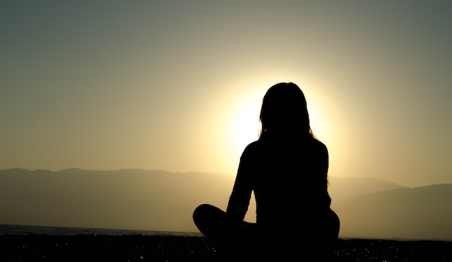 silhouette of a woman sitting looking out at water at sunset