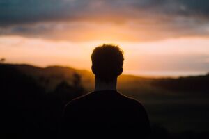 silhouette photo of a man looking out at a dark sunset sky
