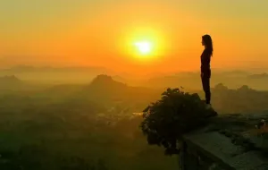 woman-standing-on-a-rock-overlooking-hills-at-sunset