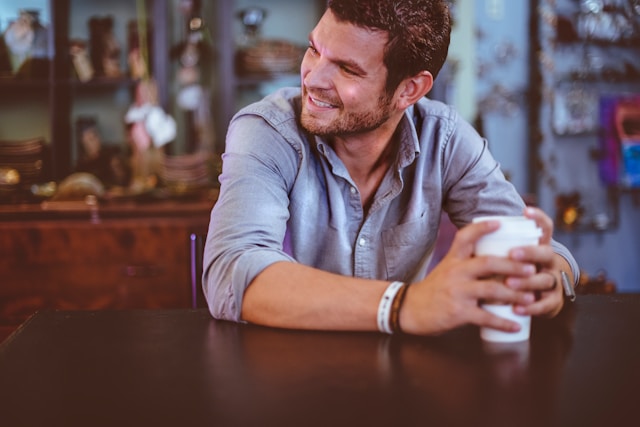 photo of a man sitting at a table holding a to go coffee cup